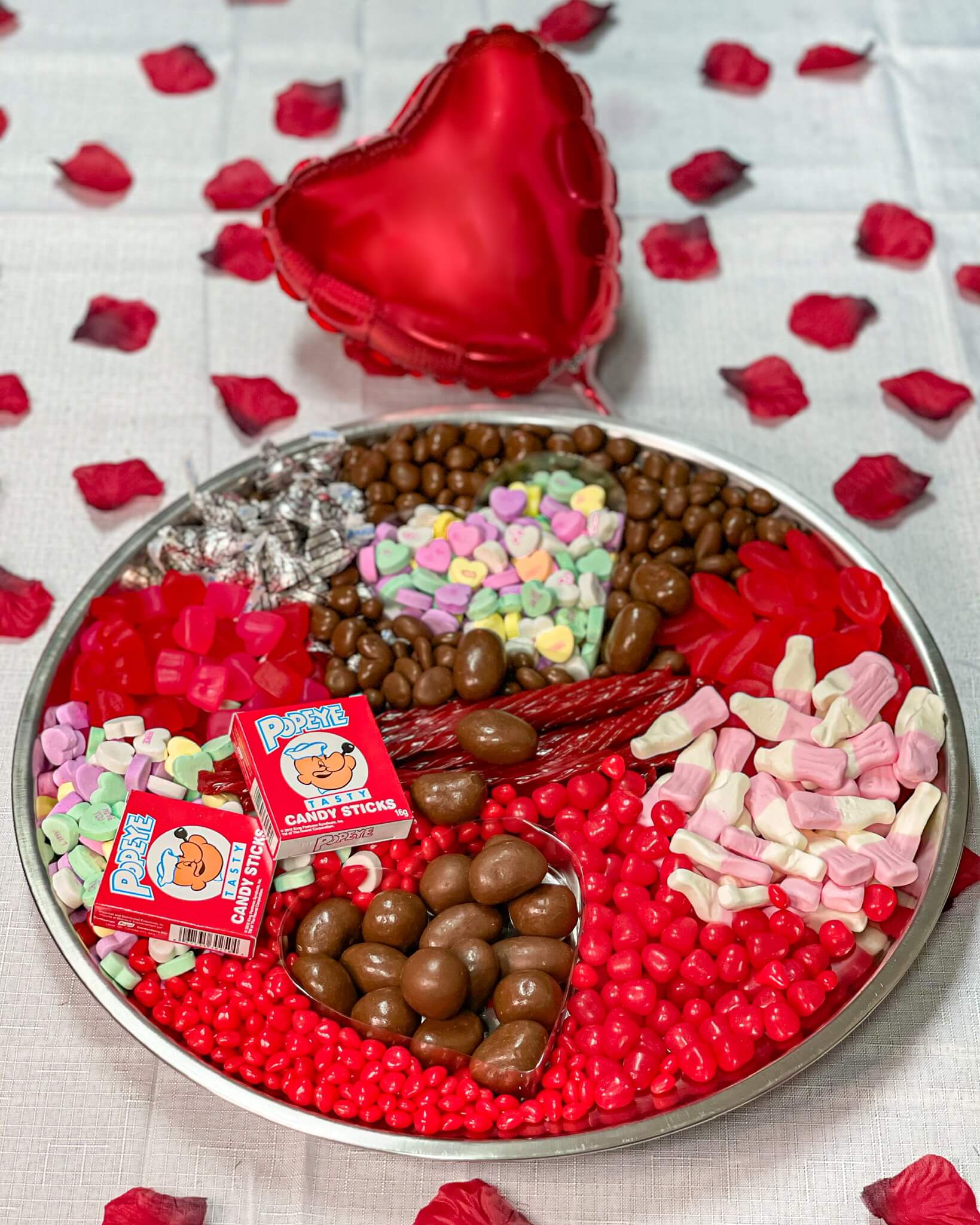 Cured catering candy tray with candy hearts, licorice, hershey’s kisses with rose petals in background