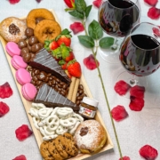 Cured catering valentine’s day dessert tray with donuts, macarons, cake and rose petals and wine